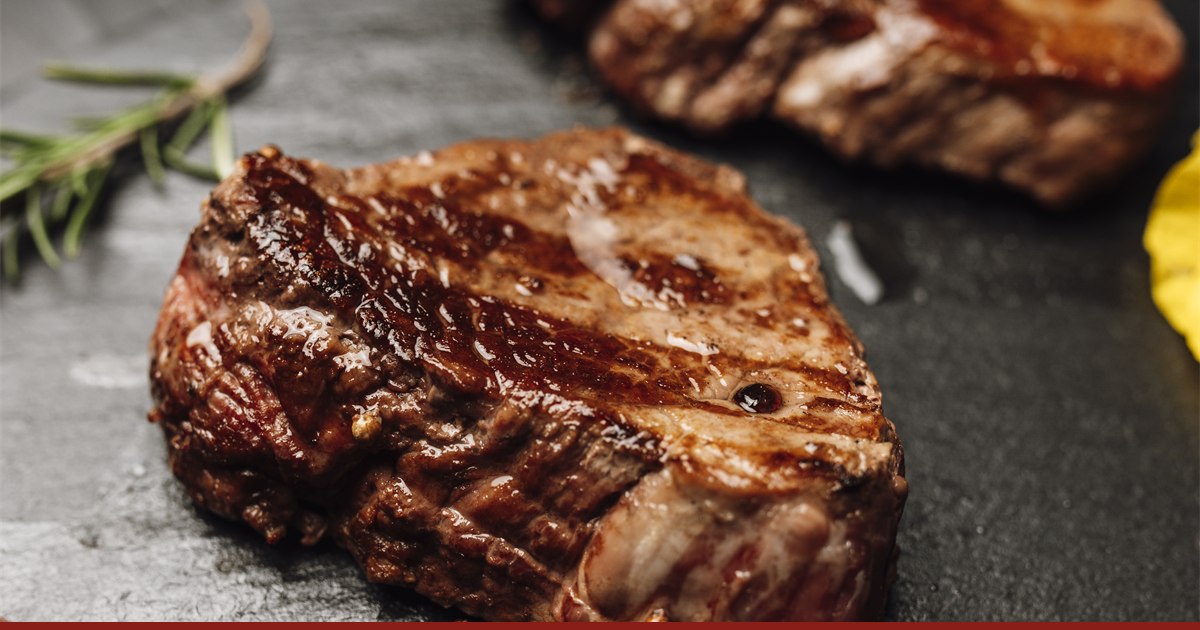 Grilled beef steaks on a black slate board with a sprig of rosemary